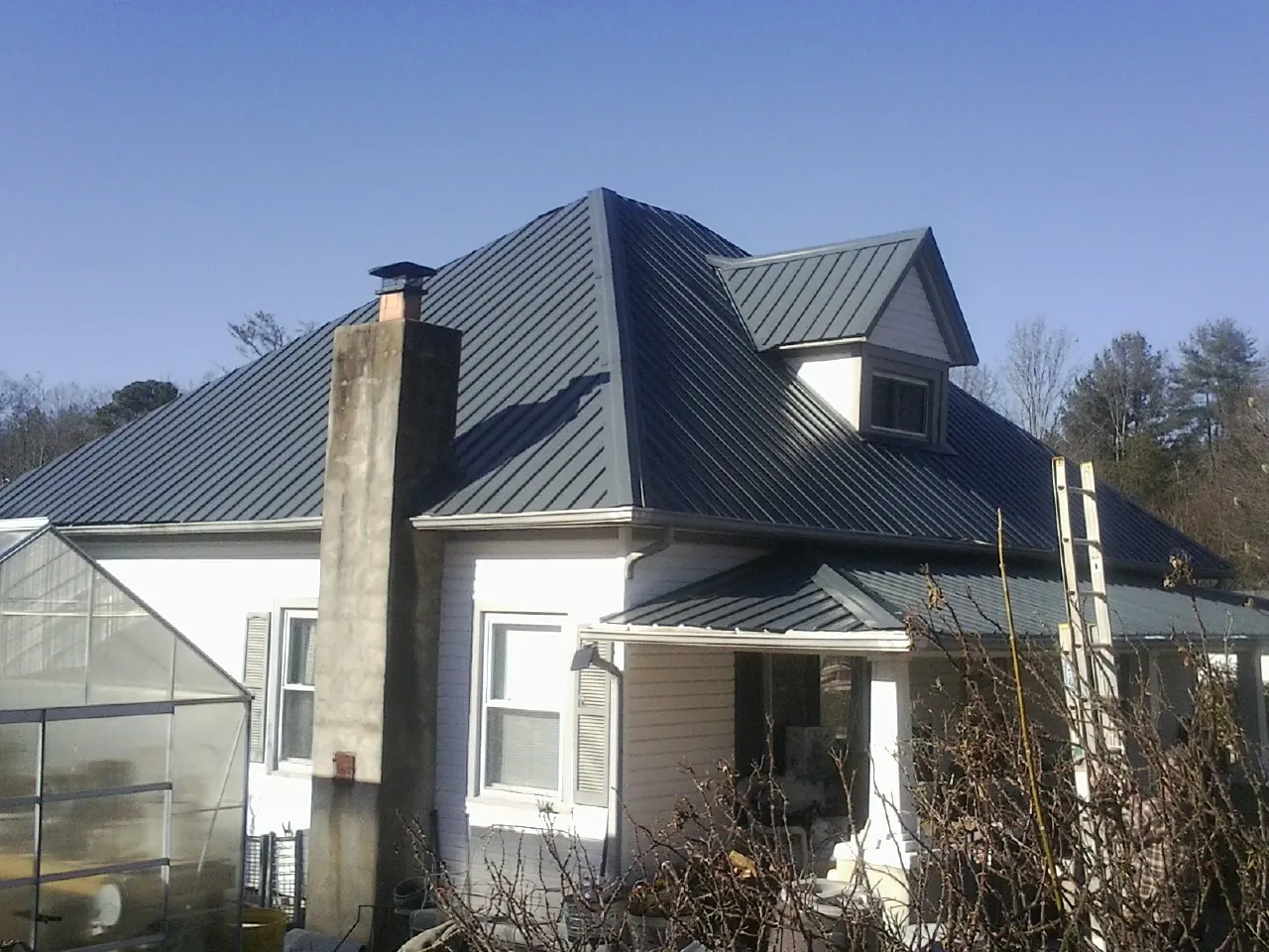 Dark blue standing seam metal roof on a white farmhouse with dormer — Slate & Tile Roof Repair by Roofing Brothers in Trussville