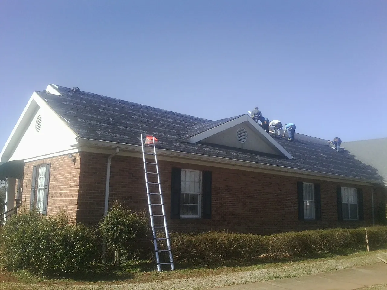 Crew tearing shingles off a brick ranch roof with a ladder set — Emergency Roof Repair work by our crew in Trussville