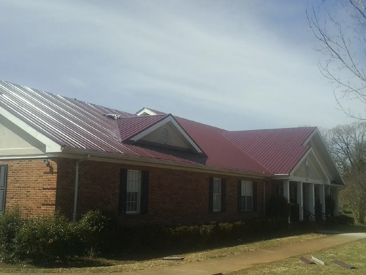 Red metal roof with gabled entries on a long brick building, from a Hail Damage Roof Repair job in Trussville