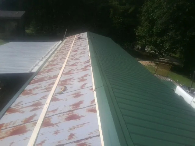 Old rusted panels beside newly installed green metal roofing — Wind Damage Roof Repair by Roofing Brothers in Trussville