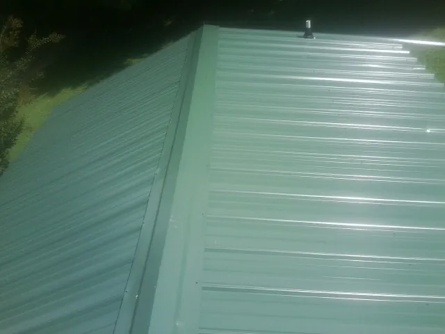 New green metal panels meeting at the ridge of a roof — Flat Roof Repair work by our crew in Trussville