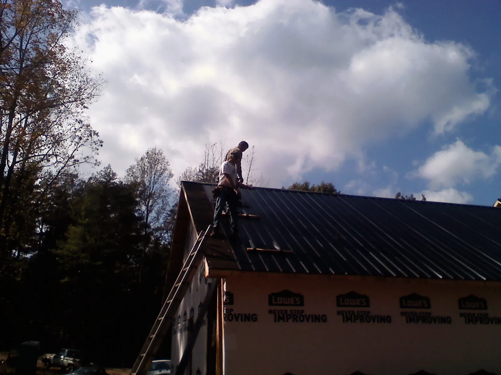 Roofer fastening dark metal panels high against a cloudy sky, from a Roof Inspection job in Trussville