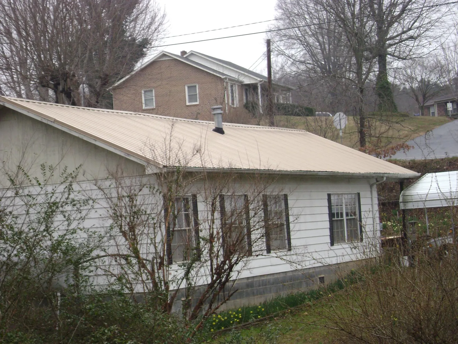 Tan metal roof on a white sided house set into a hillside — Commercial Roofing by Roofing Brothers in Trussville