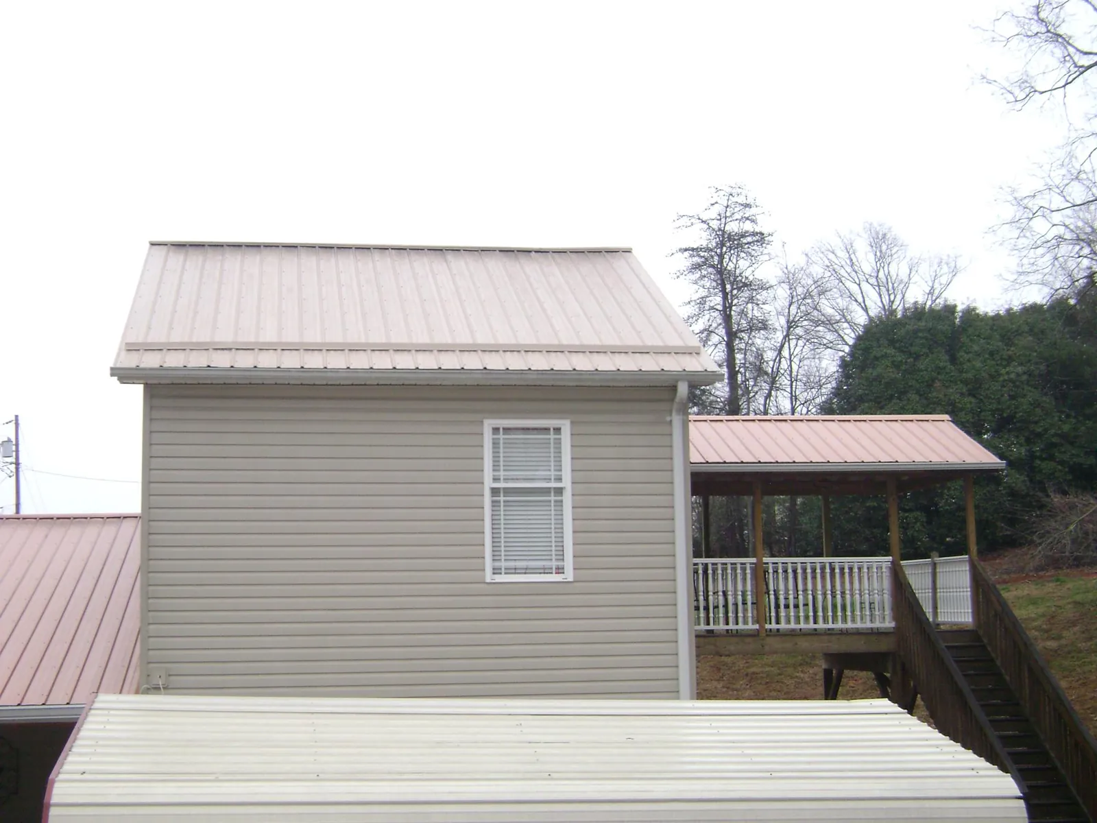 Tan metal roofs on a two story addition and attached porch, from a Roof Replacement job in Trussville